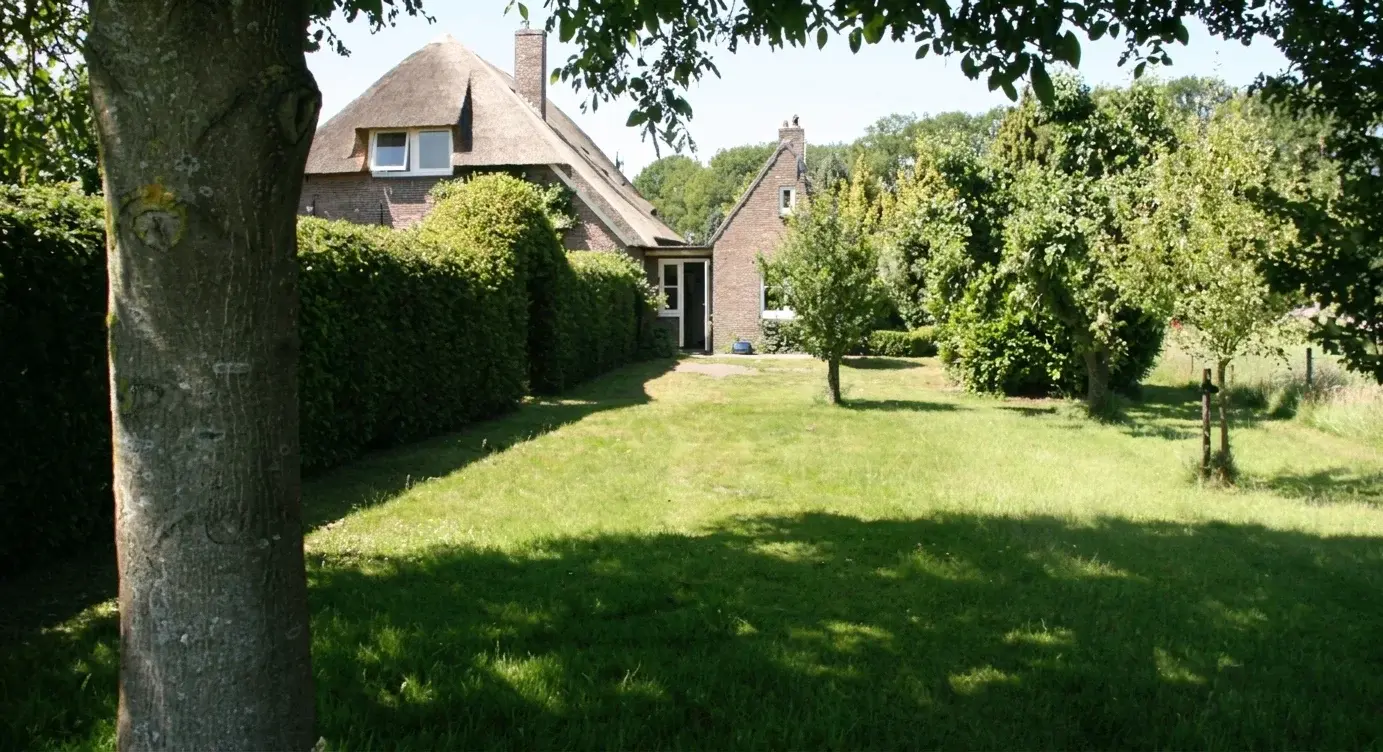 Het Bakhuis gezien over het gazon, met de hoge heg en de fruitbomen in de tuin